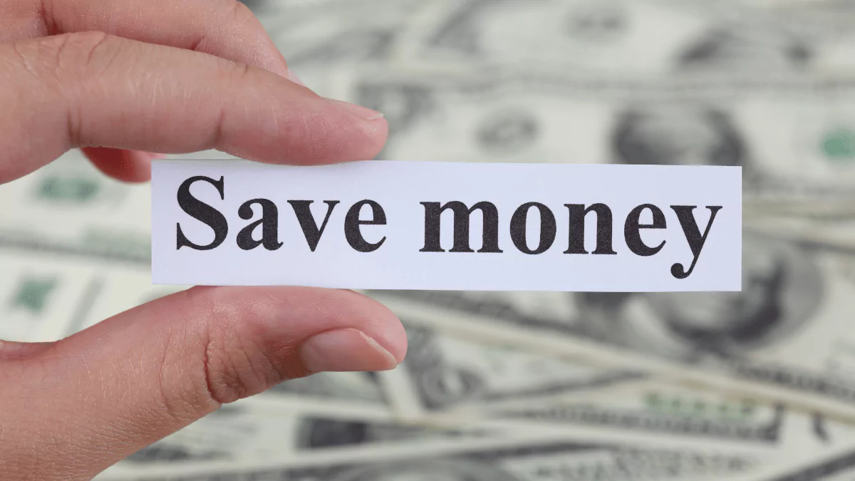A woman holds a small note reading "Save money" with U.S. dollar bills in the background. Close-up view