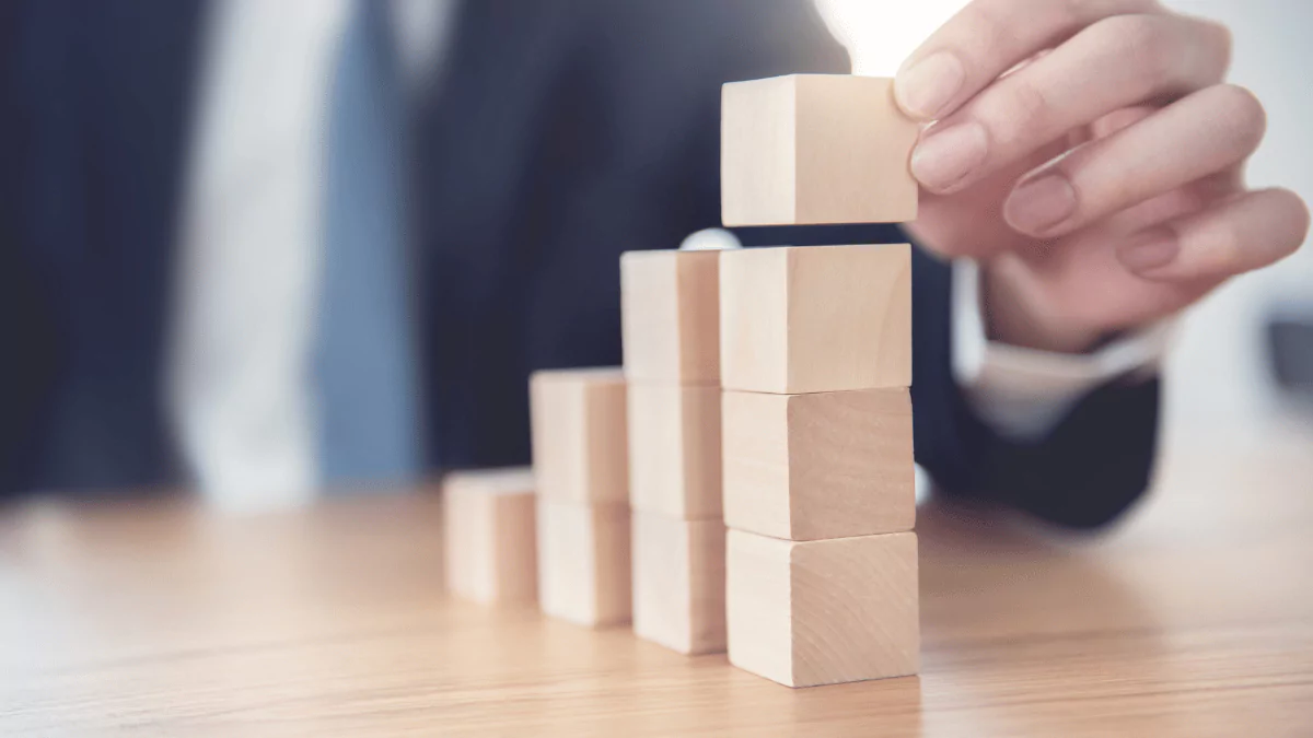 Close-up of a businessman’s hand stacking wooden cubes as steps, symbolizing the path to business success