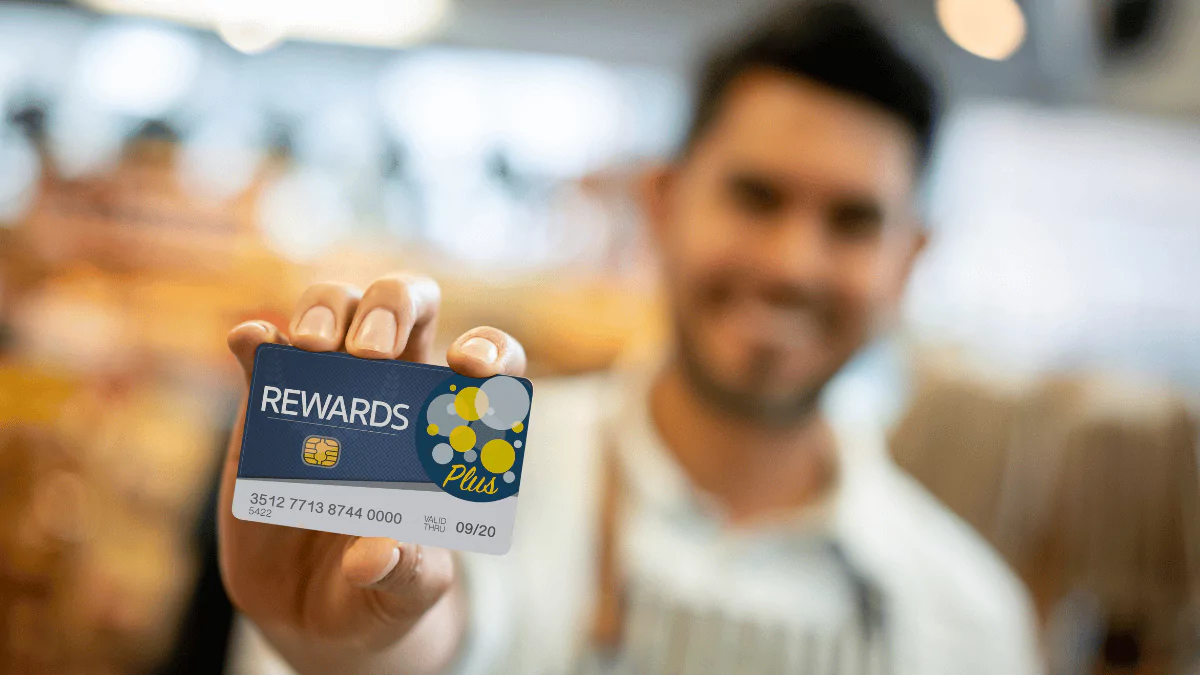 Salesman at a grocery store holding a loyalty card up front. Focus on foreground.