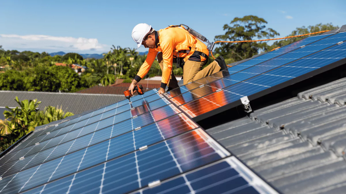 Solar panel technician with drill installing solar panels On a house roof, on a sunny day.